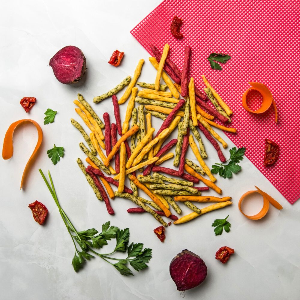 Colorful vegetable sticks on a white surface with a pink mat in the background