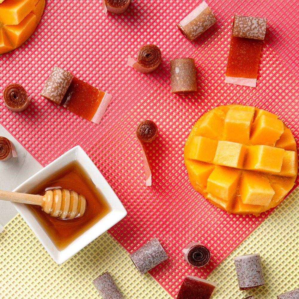 Mango cubes, honey, and small desserts on a pink and yellow checkered background