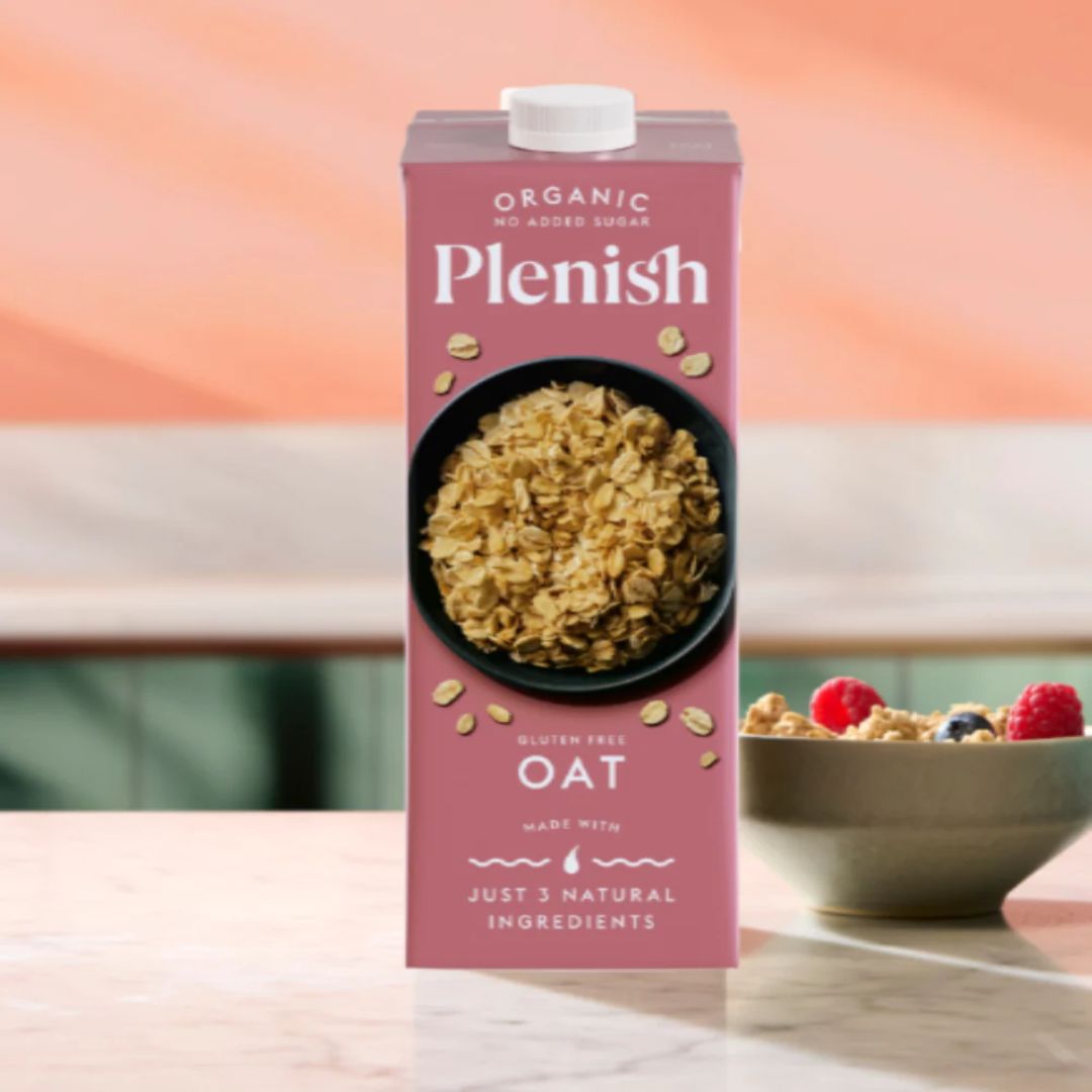 Plenish organic oat milk carton with a bowl of cereal and berries on a wooden table.
