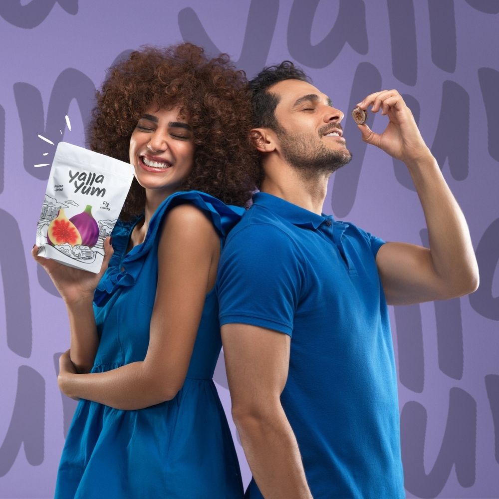 Two people in blue shirts with a Yum Yum snack package against a purple background
