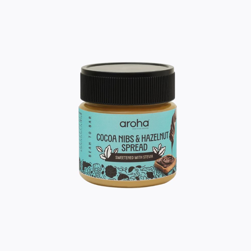 A jar of aroha Cocoa Nibs & Hazelnut Spread on a clean white background. The jar has a black lid and a light blue label with brown and black text and illustrations.