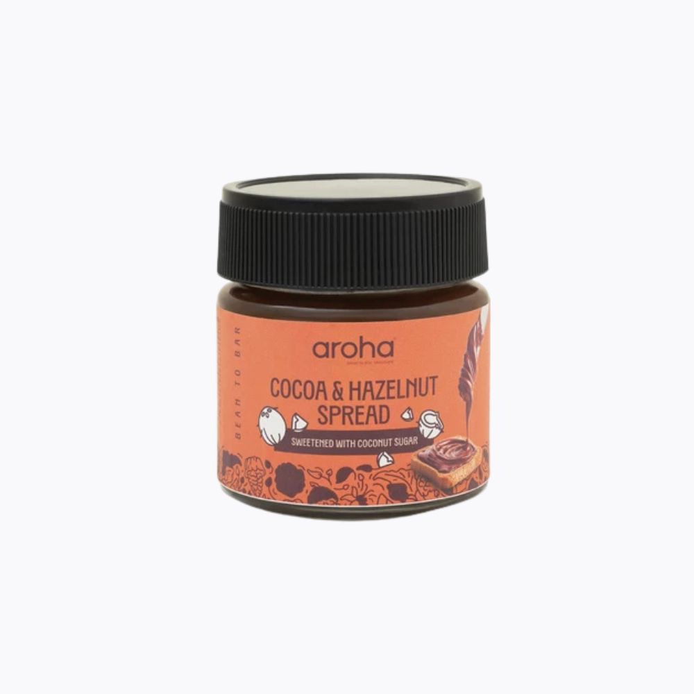 A small jar of Aroha Cocoa & Hazelnut Spread on a clean white background. The jar has a black screw cap and a terracotta-colored label with illustrations of cocoa beans and chocolate.