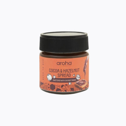 A small jar of Aroha Cocoa & Hazelnut Spread on a clean white background. The jar has a black screw cap and a terracotta-colored label with illustrations of cocoa beans and chocolate.