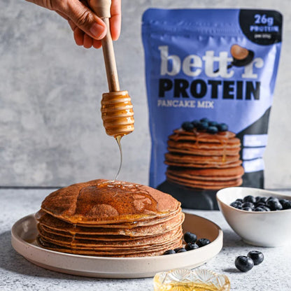 Stack of pancakes with honey being drizzled, protein mix in the background