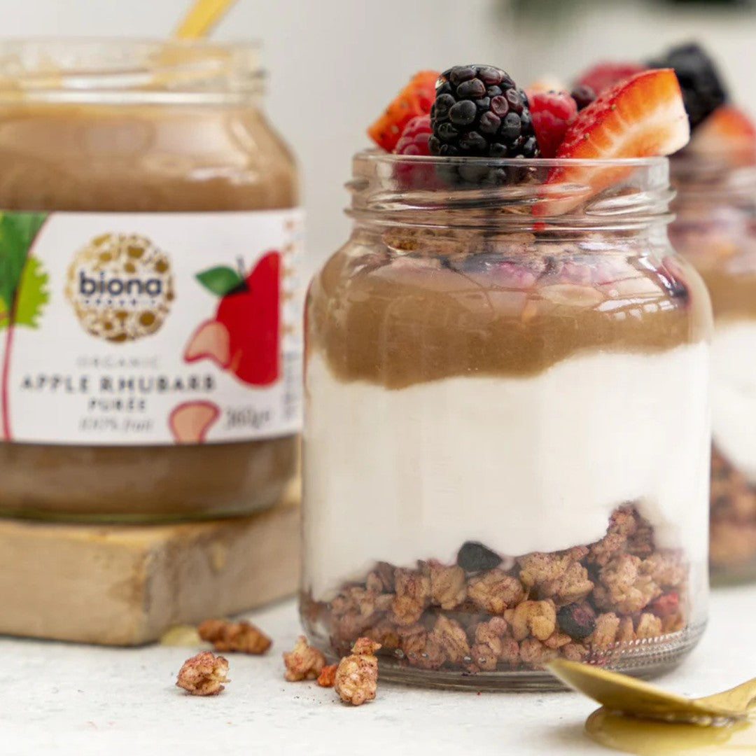 Mason jar dessert with yogurt, granola, and berries next to a jar of biona apple rhubarb puree.