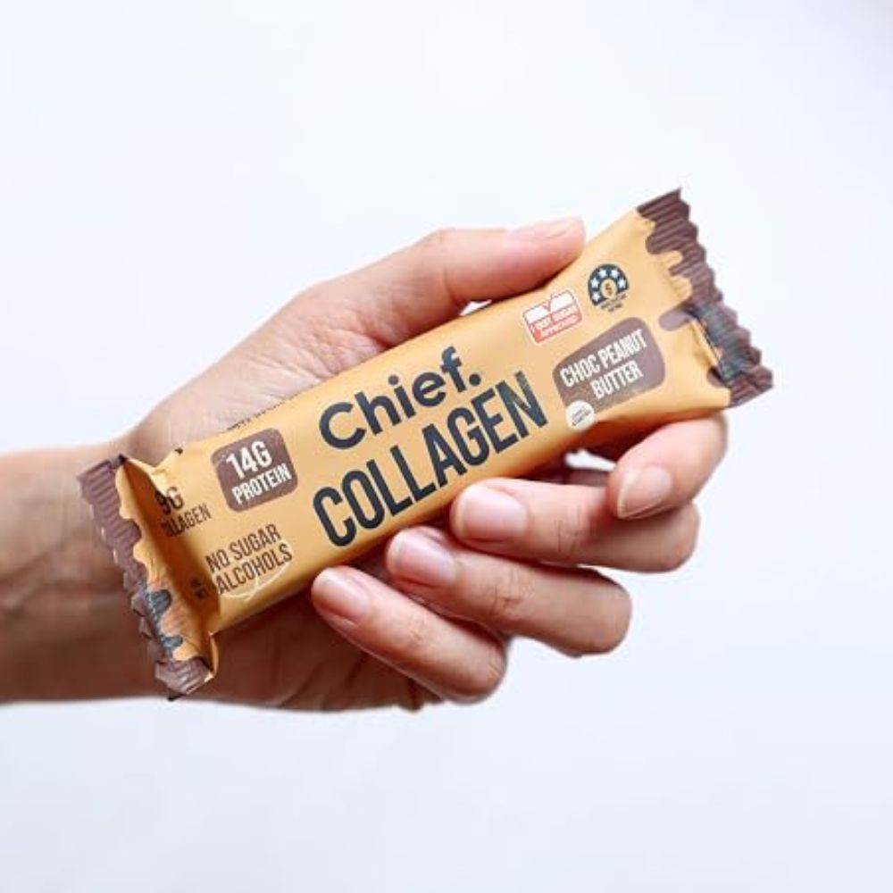 A hand holding a wrapped collagen protein bar. The wrapper is tan with dark brown text reading 'Chief Collagen' and 'Chic Peanut Butter' flavor, shown against a plain white background.