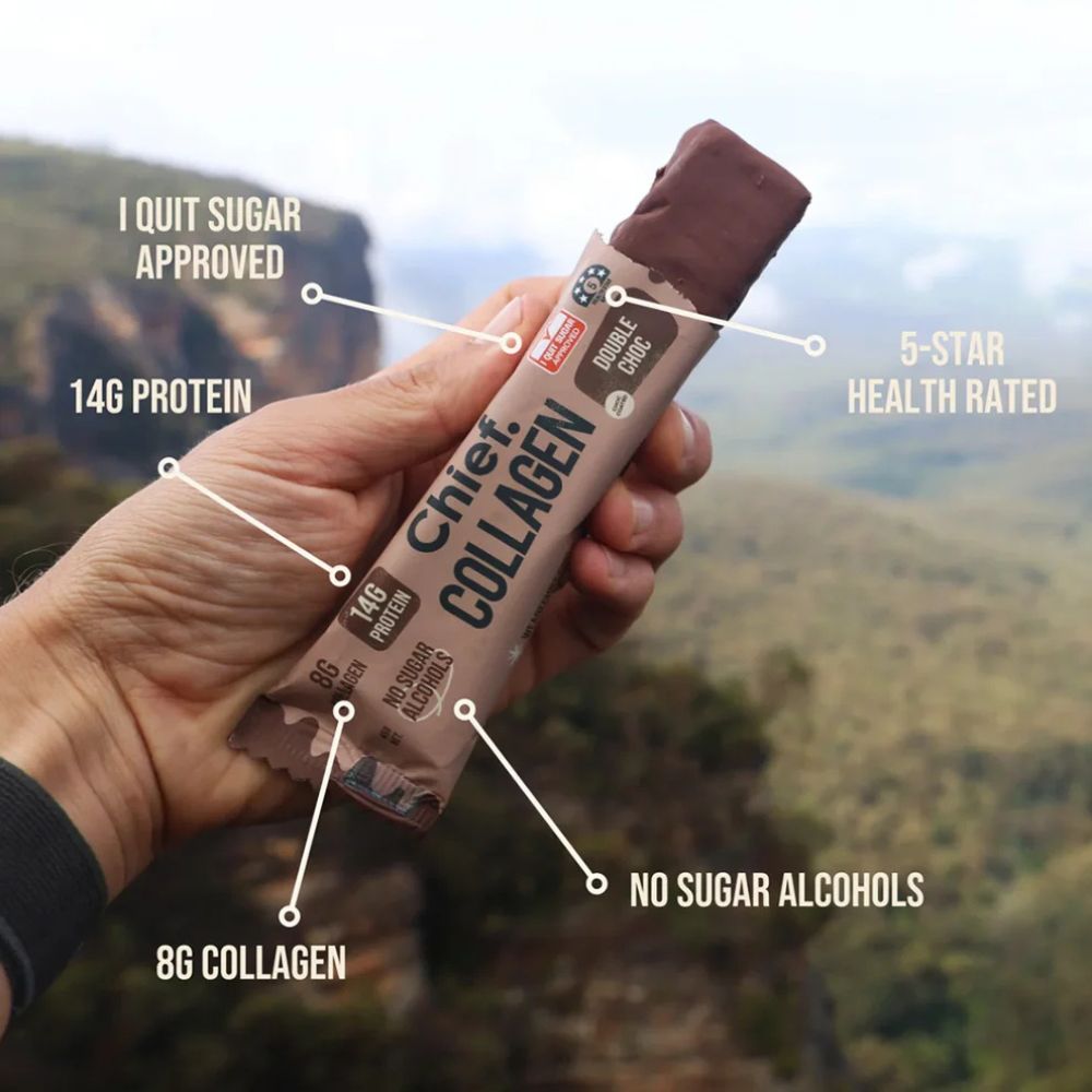 A hand holds a chocolate collagen powder stick pack against a blurred mountain landscape background. White text callouts point to the product with claims like 'I Quit Sugar Approved,' '14G Protein,' '5-Star Health Rated,' '8G Collagen,' and 'No Sugar Alcohols.