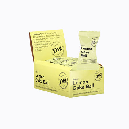 A box of Dig Naturally Lemon Cake Ball vegan snacks, showing the yellow packaging, a single wrapped ball, and several unwrapped cake balls inside the box against a white background.