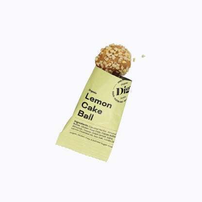 A single Dig Free Lemon Cake Ball snack on a light yellow wrapper, shown against a plain white background.