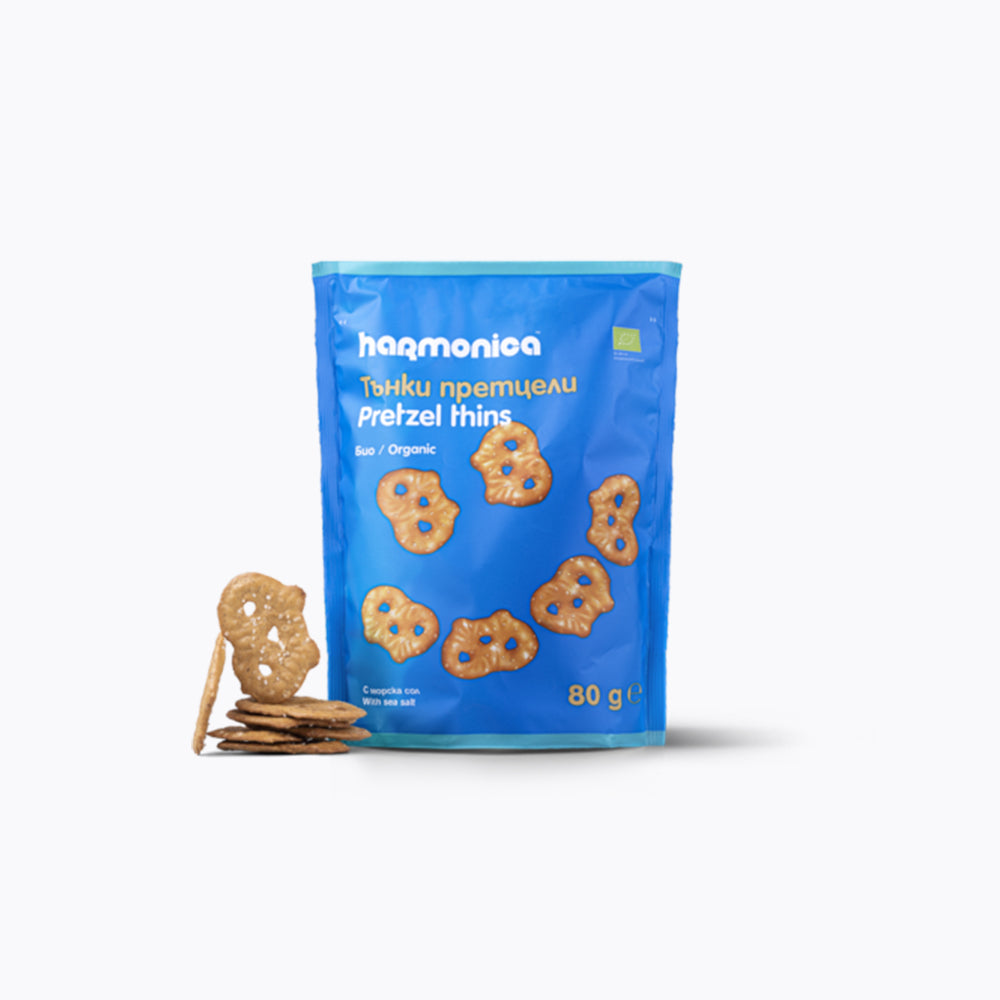 A blue package of Harmonica Wholegrain Pretzel Thins with the product visible through the transparent window. The package is labeled as dairy free, gmo free, kids approved, organic, plant based, salty fix, and vegan.