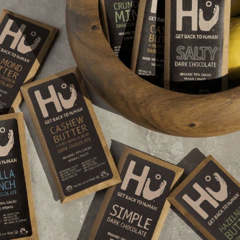 HU chocolate bars displayed around a wooden bowl on a gray surface