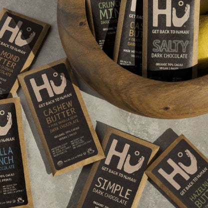 HU chocolate bars displayed around a wooden bowl on a gray surface