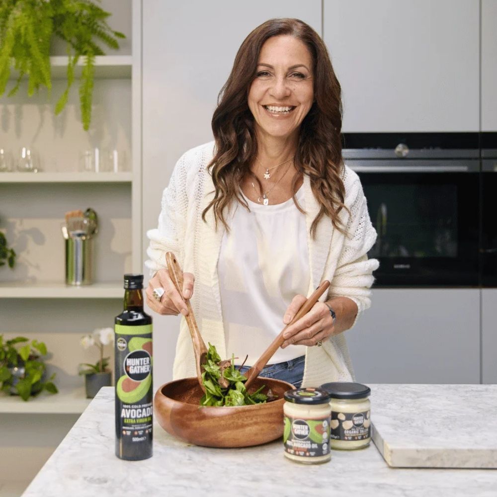 Woman preparing a salad in a kitchen with ingredients and a bottle on the counter.