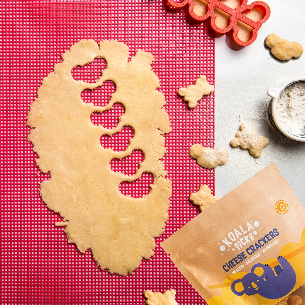 Cookie cutter with shaped cookie on a red mat, surrounded by more cookies and a package of Koala Biscuits.
