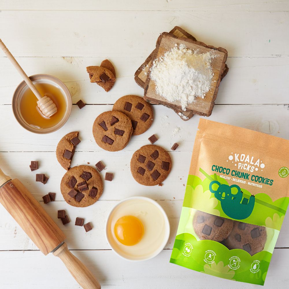 Choco chunk cookies with a packaging on a wooden surface with ingredients like honey, eggs, and flour.