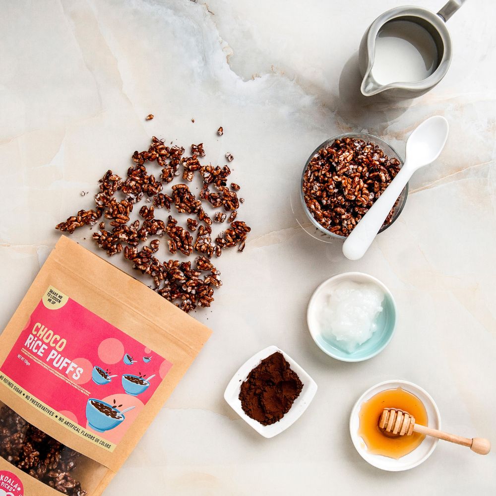 Choco rice puffs with packaging, milk, honey, and a spoon on a marble surface