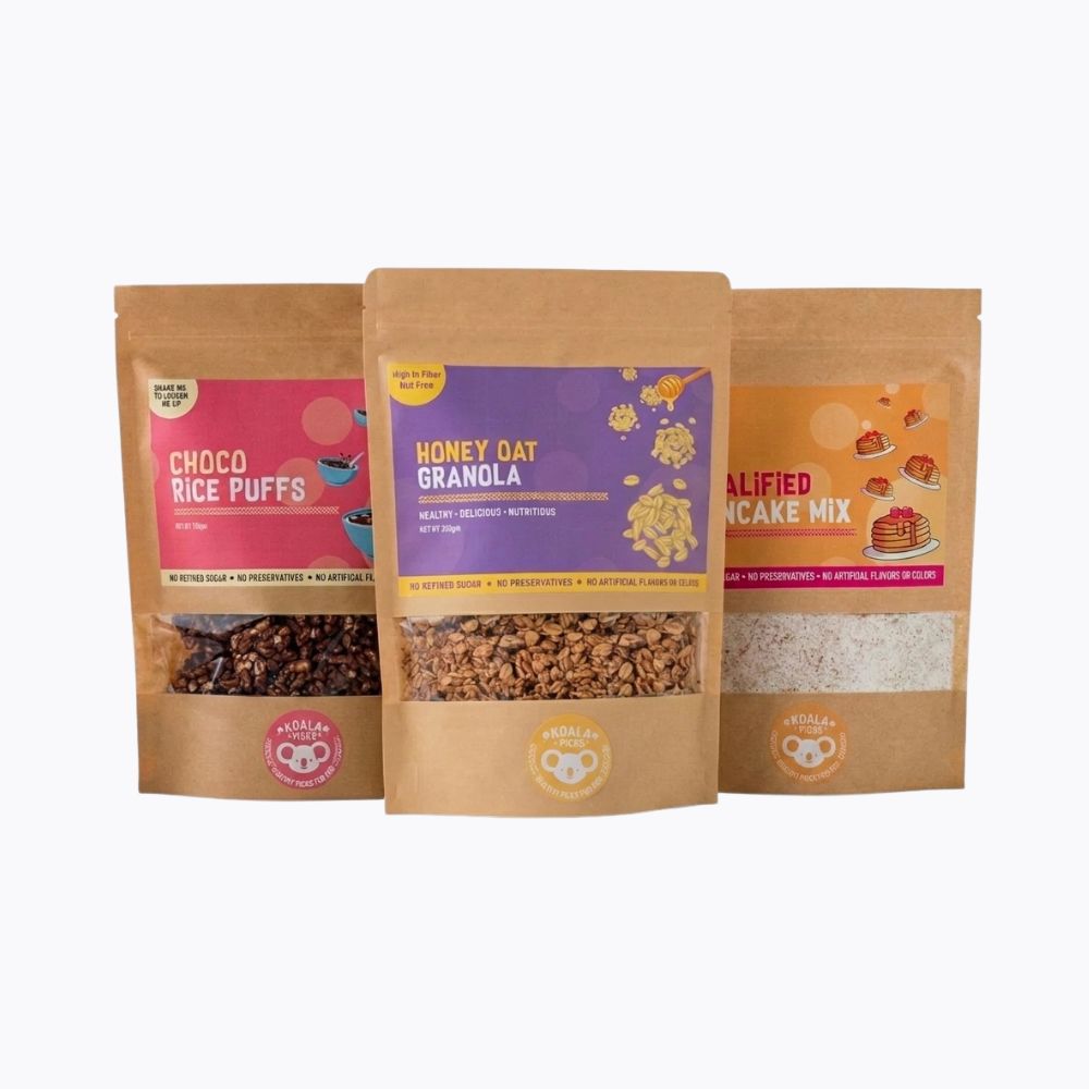 Three stand-up pouches of NutriKids snack mix products arranged side by side on a light gray background: Choco Rice Puffs, Honey Oat Granola, and Calified Pancake Mix.
