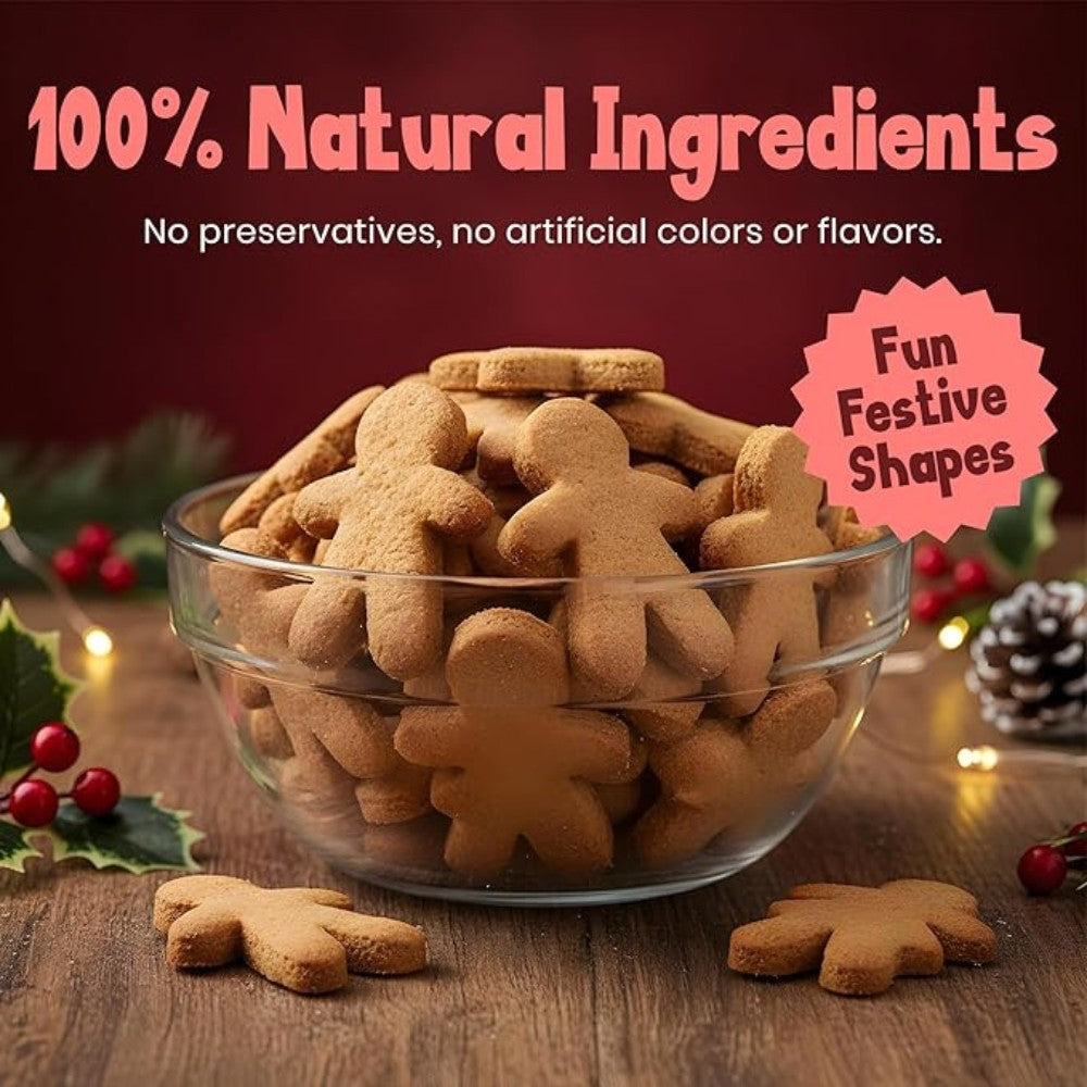 Glass bowl filled with gingerbread-shaped dog treats on a wooden surface with festive decorations.