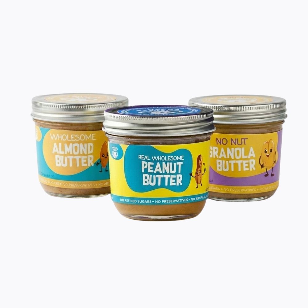 Three jars of baby food spread arranged together on a light gray background: almond butter on the left, peanut butter in the center, and granola on the right. The jars have silver metal lids and colorful labels with cartoon characters.