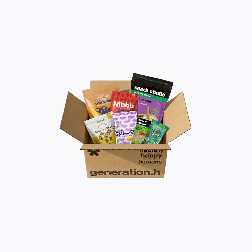 A cardboard gift box filled with assorted packaged snacks and treats, photographed on a plain light gray background. The box is branded 'generation.
