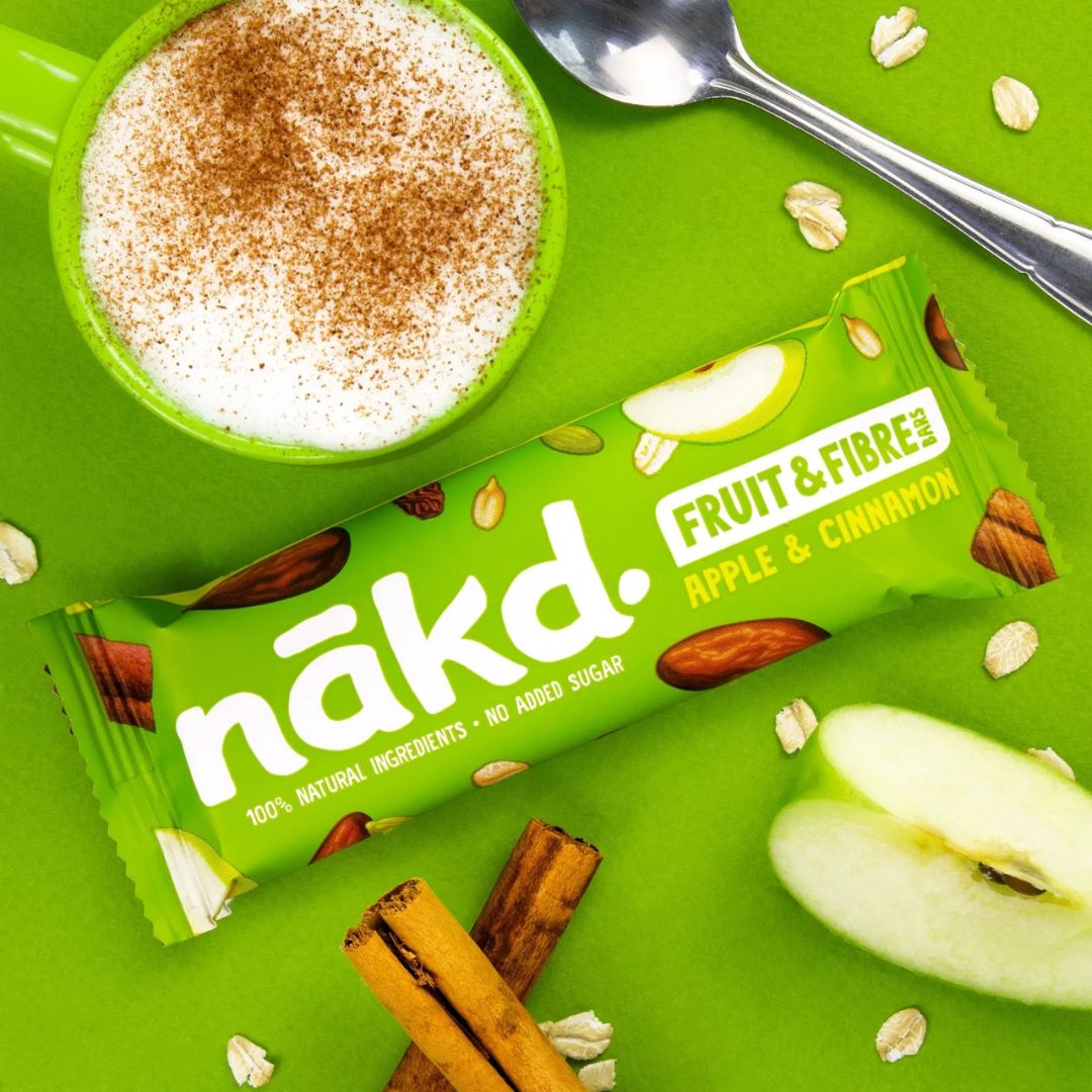 Nakd Apple & Cinnamon fruit and fiber bar on a green background with a bowl of cinnamon spice mix.
