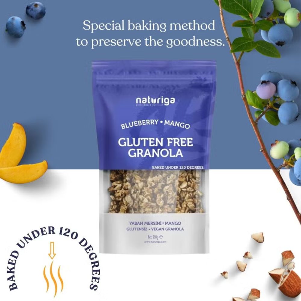 A package of Naturiga Blueberry + Mango Gluten Free Granola, styled with blueberries, mango slices, and almonds on a split blue and white background with promotional text.