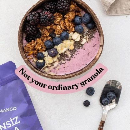 A bowl of pink smoothie topped with blackberries, blueberries, granola, and coconut flakes, styled on a light surface with a purple pouch, a spoon, and a text overlay reading 'Not your ordinary granola'.