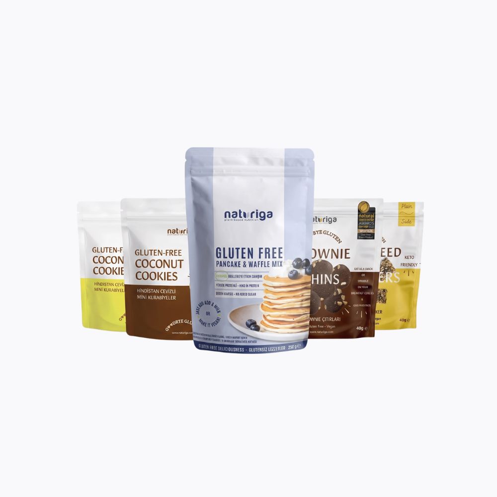 Four stand-up pouches of Natur Riga gluten-free snacks and cookies displayed against a plain white background, with the central blue-and-white pouch for Gluten Free Pancake & Baked Breakfast Mix in front.