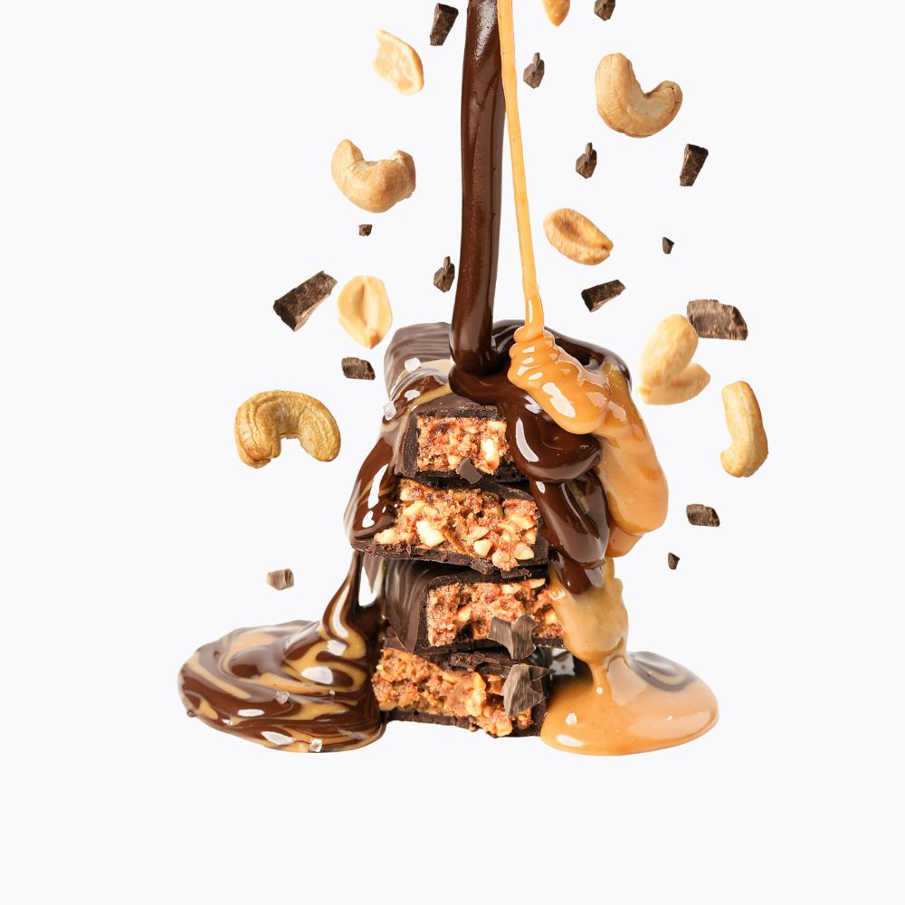 Chocolate and peanut butter dessert with cashews being drizzled over it on a white background