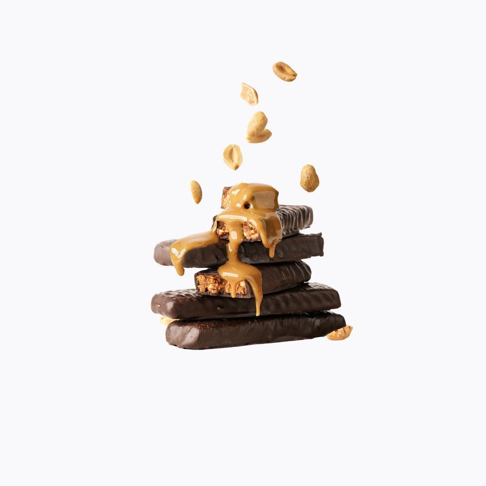 Stack of chocolate bars with peanut butter being poured over them on a white background
