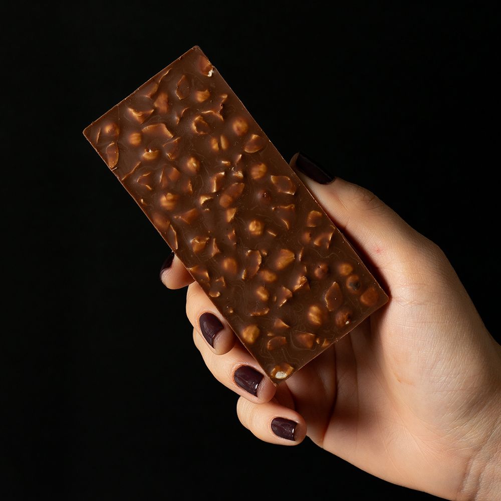 Hand holding a chocolate bar with a textured surface against a black background