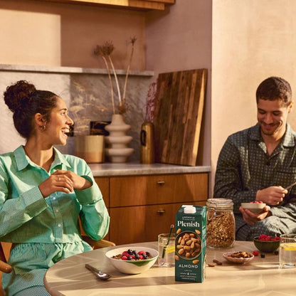 Two people in a kitchen with a box of Plenish Almond Crunch on the table.