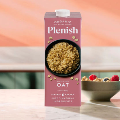 Plenish organic oat milk carton with a bowl of cereal and berries on a wooden table.