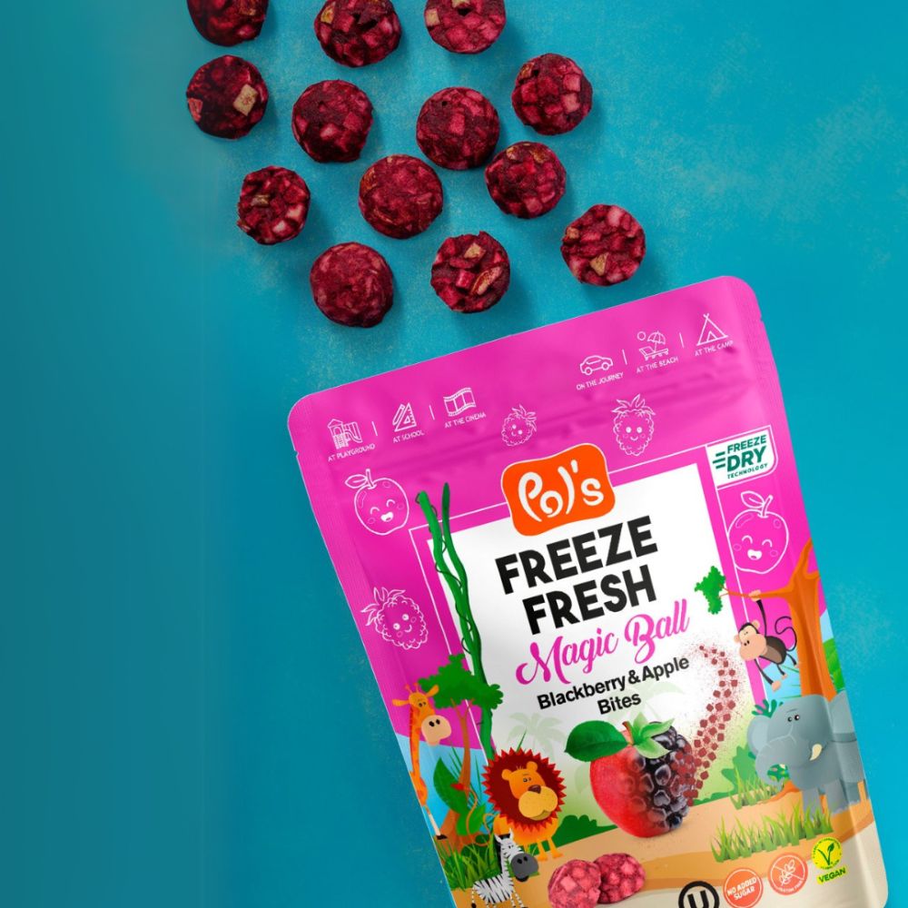 A stand-up pouch of Rol's Freeze Fresh Magic Ball Blackberry & Apple Bites is shown on a bright turquoise background with several red berry disc bites scattered above it. The packaging is predominantly pink and white with colorful animal illustrations and product details.