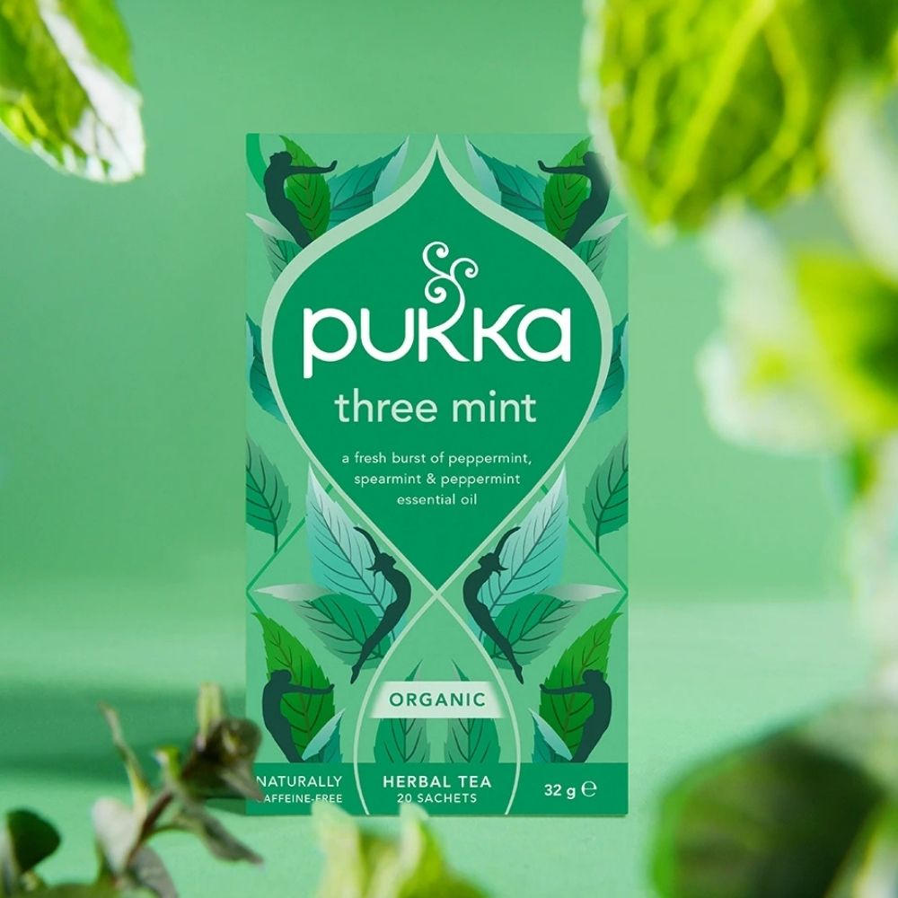 Pukka three mint herbal tea packaging on a green background with mint leaves.