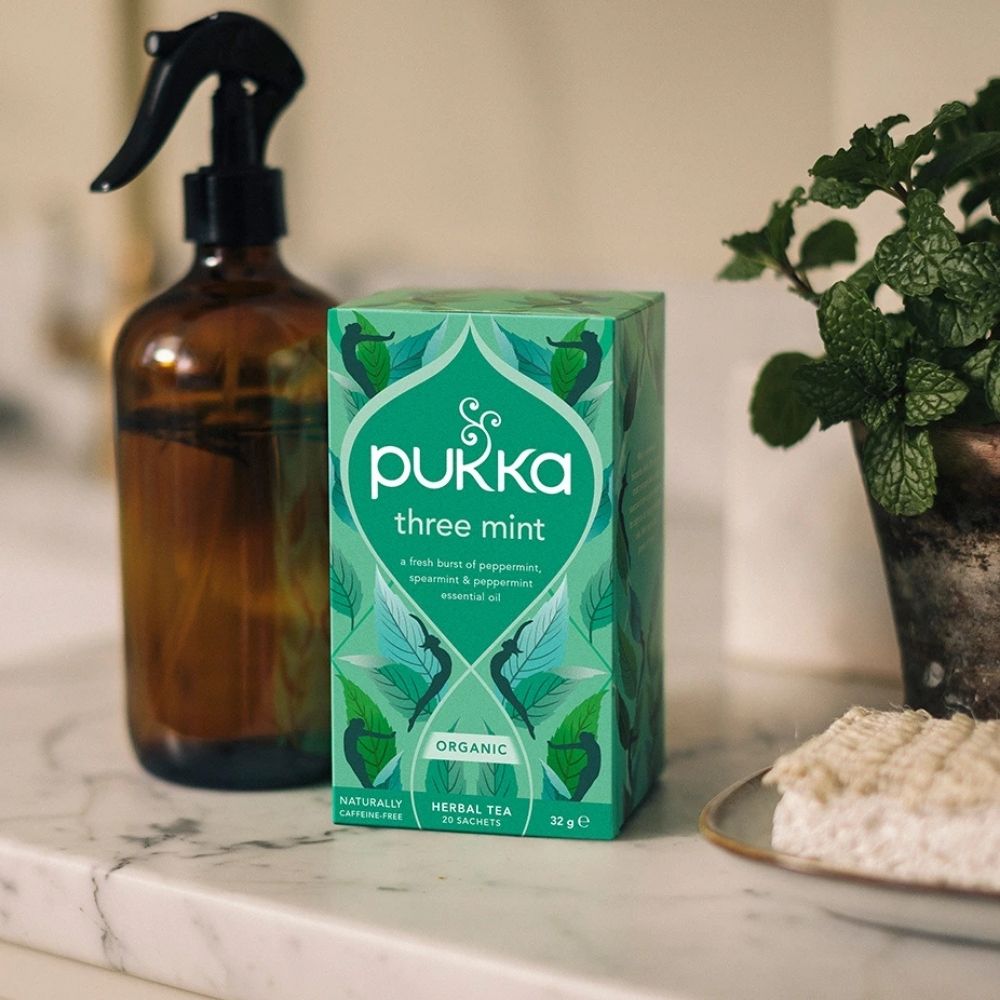 Pukka three mint tea box on a marble surface with a plant and bottle in the background