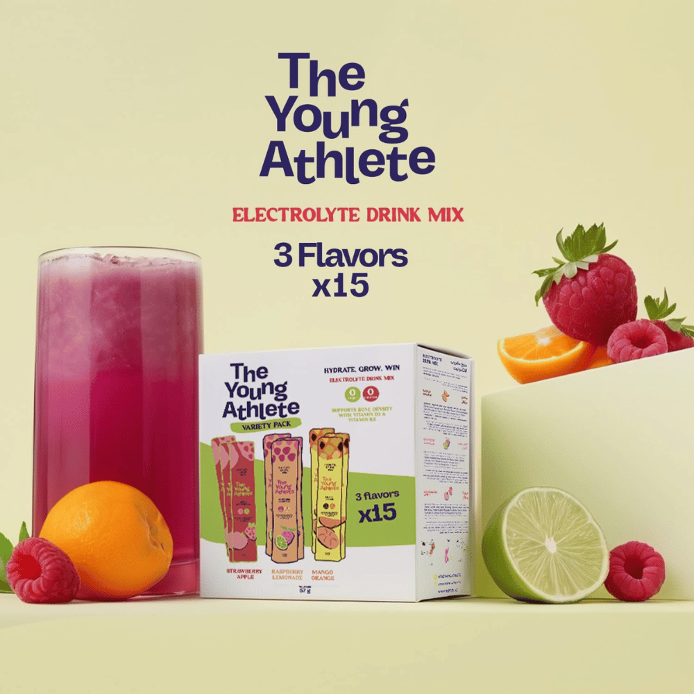 The Young Athlete electrolyte drink mix packaging with a glass of pink drink and fruit on a light green background.