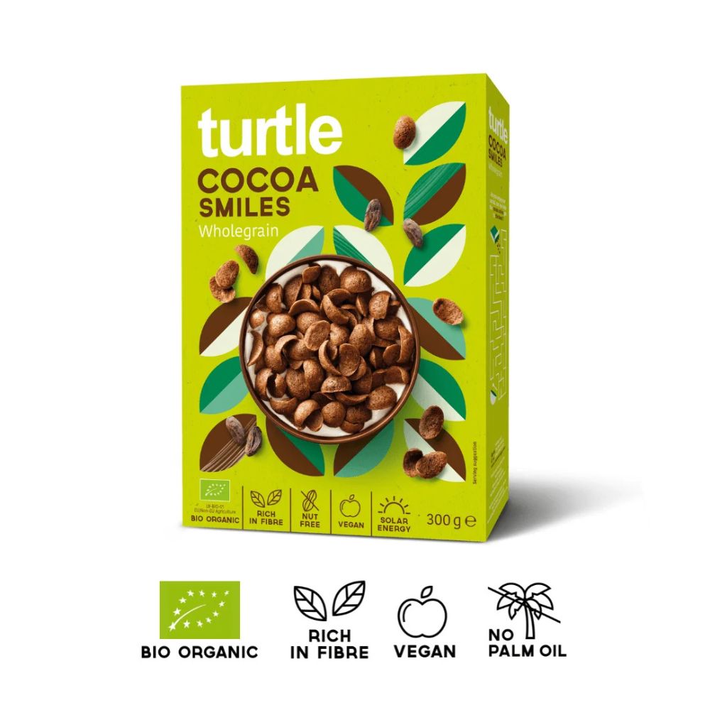A 300g box of turtle brand Cocoa Smiles Wholegrain cereal, featuring a bright lime green packaging design with illustrations of cocoa beans and leaves. Below the box, four black-and-white icons highlight key product attributes: Bio Organic, Rich in Fibre, Vegan, and No Palm Oil.