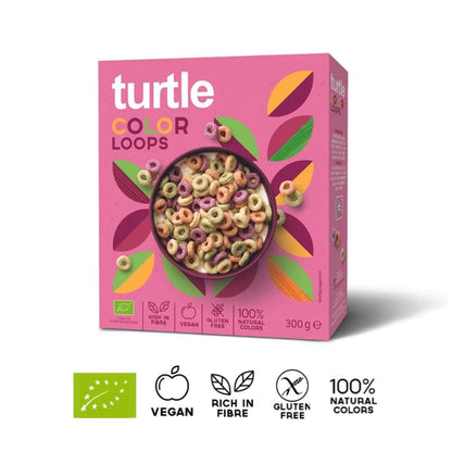 A 300 g box of turtle Color Loops cereal on a white background, featuring a pink box with multicolored leaf graphics and a bowl of colorful ring cereal. Below the box are certification and feature icons for organic, vegan, rich in fibre, gluten free, and 100% natural colors.