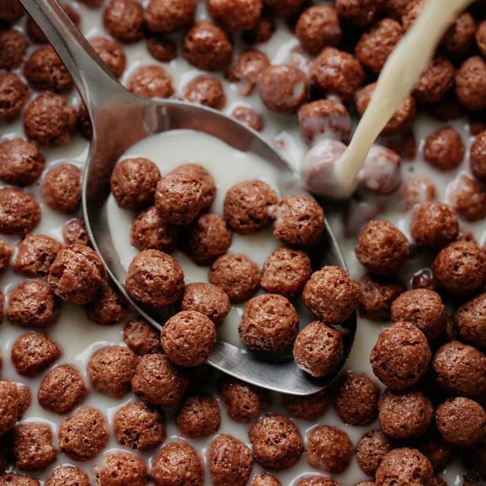 Chocolate cereal being poured into a spoon with milk