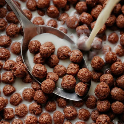 Chocolate cereal being poured into a spoon with milk
