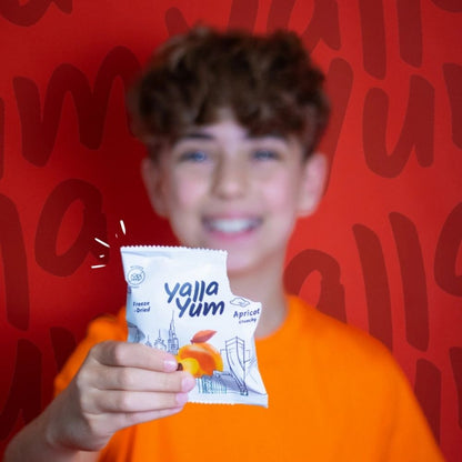 Person holding a 'Yalla Yum' snack packet in front of a red background with text.