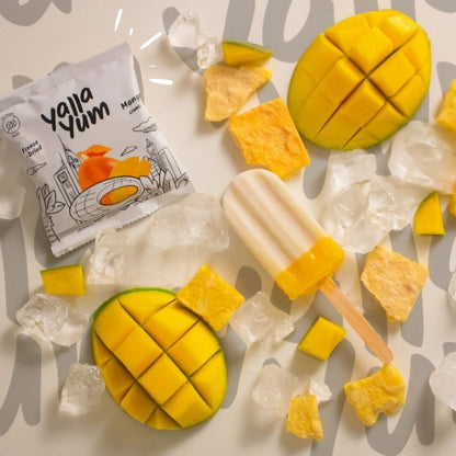 Mango popsicle with chunks of mango and a Yalla Yum packaging on a light background