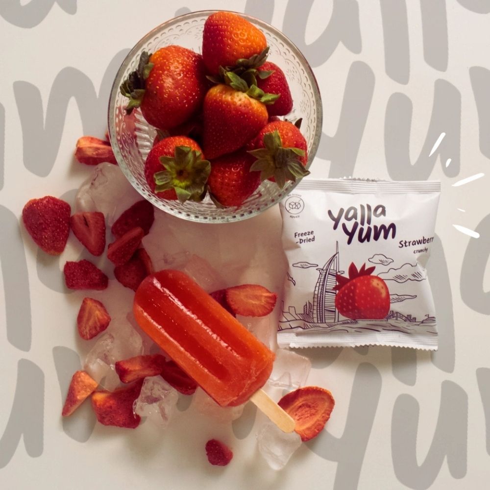 Strawberries, a popsicle, and a Yella Yum strawberry candy package on a light background.