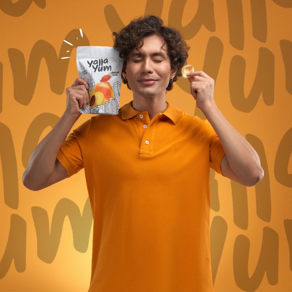 Man in orange shirt holding Yola Yum snack packet and cracker against an orange background